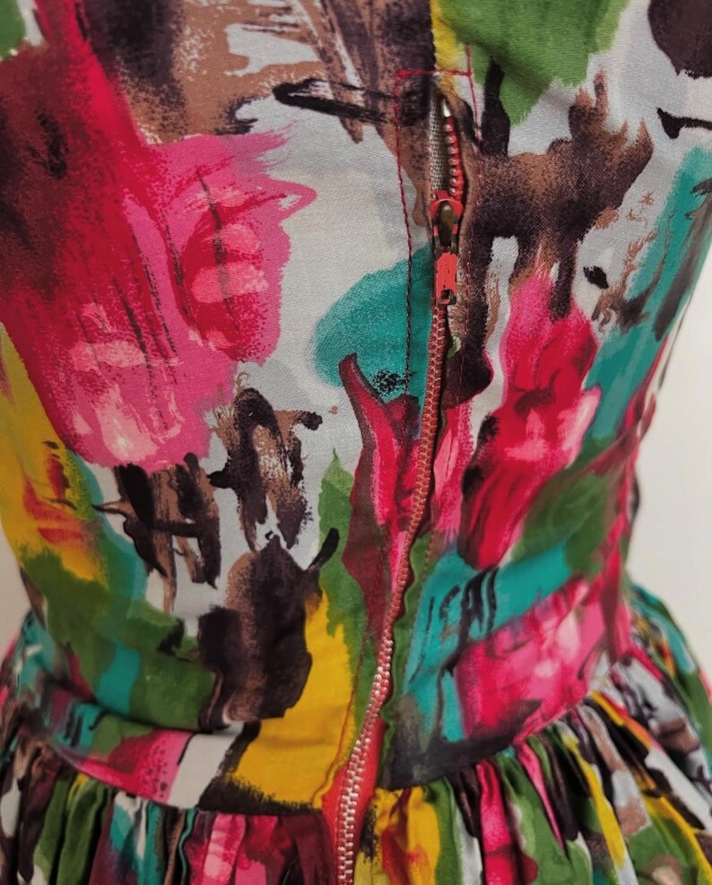 May include: A colorful dress with a zipper closure. The dress has a bright abstract print with shades of pink, green, yellow, and brown.