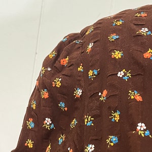 May include: A brown fabric with a small floral pattern in shades of blue, yellow, orange, and white.