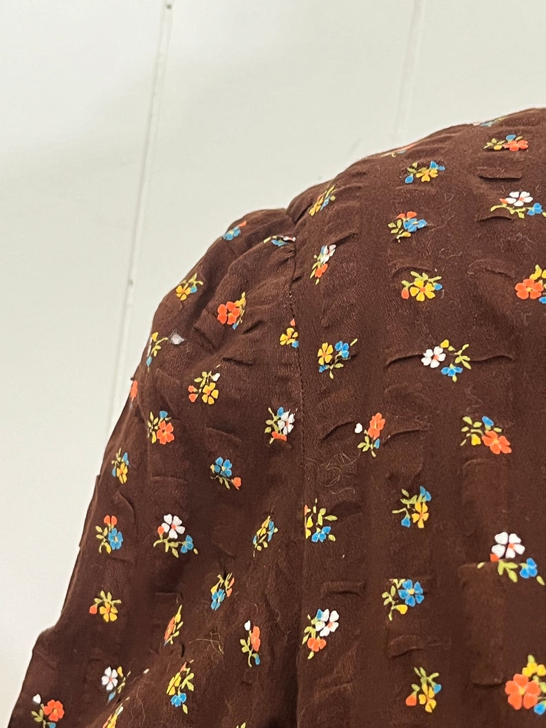 May include: A brown fabric with a small floral pattern in shades of blue, yellow, orange, and white.