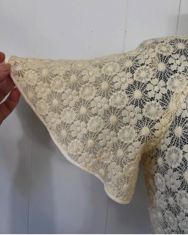 May include: A white lace top with a floral pattern. The sleeves are short and have a scalloped edge.
