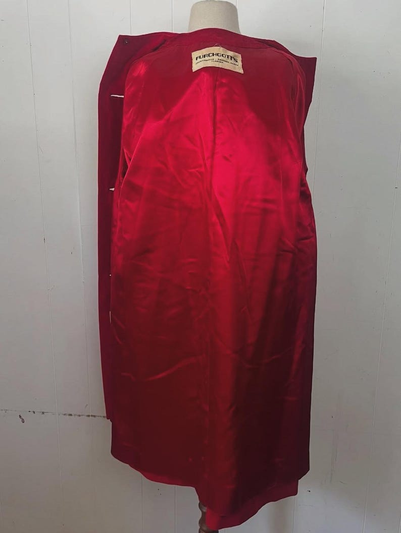 May include: A long, red coat with a satin lining. The coat is displayed on a mannequin. The interior lining is a bright red color. A tag inside the coat reads "FURCHGOTTS".