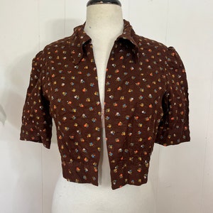 May include: A brown cropped jacket with a floral print. The jacket has a collar and short sleeves.