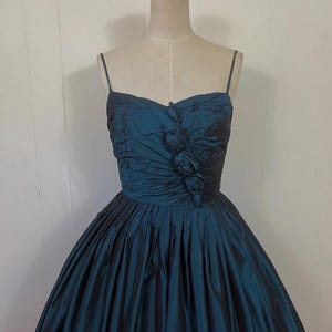 May include: A teal vintage dress with a sweetheart neckline and spaghetti straps. The bodice is ruched with floral detailing, and the full skirt is pleated. The dress is displayed on a mannequin.