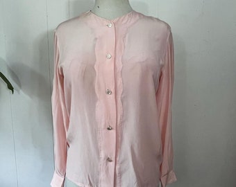 May include: A pale pink, long-sleeved blouse with a button-up front and a scalloped trim detail. The blouse has a mandarin collar and is made of a lightweight fabric.