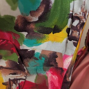 May include: Close-up of a colorful fabric with abstract brushstrokes in shades of red, pink, green, blue, yellow, and brown. The fabric has a white background and a subtle texture.