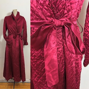 May include: A quilted, claret-coloured robe with a matching tie belt. The robe features a shawl collar, long sleeves, and pockets. The fabric has a diamond pattern.