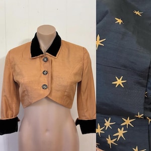 May include: A cropped tan jacket with a black velvet collar, cuffs, and three decorative buttons. The jacket has three-quarter sleeves. A separate panel shows a dark blue fabric with gold star embroidery.