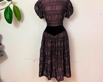 May include: A purple and black striped dress with a black velvet waistband. The dress has a fitted bodice and a full skirt.