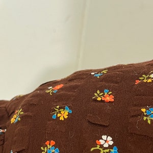 May include: Brown fabric with a floral pattern. The flowers are small and multi-colored, including orange, yellow, blue, and white.