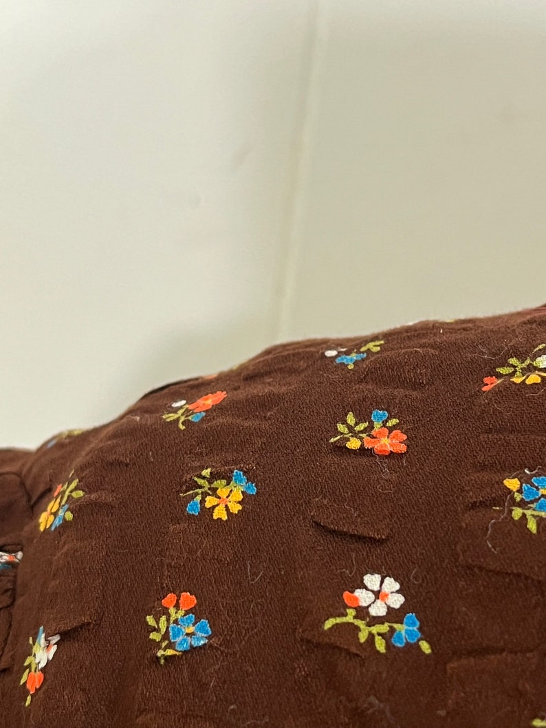 May include: Brown fabric with a floral pattern. The flowers are small and multi-colored, including orange, yellow, blue, and white.