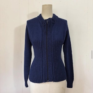 Könnte beinhalten: Ein marineblauer Vintage-Reißverschluss-Pullover mit gerippter Struktur. Der Pullover hat eine taillierte Taille und lange Ärmel. Er hat einen hohen Kragen mit Krawattendetail und einen durchgehenden schwarzen Reißverschluss. Der Pullover wird auf einer Schaufensterpuppe präsentiert.