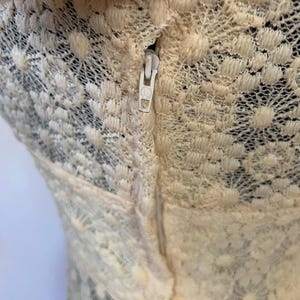May include: A close-up of a cream-colored lace garment with a zipper running down the back.