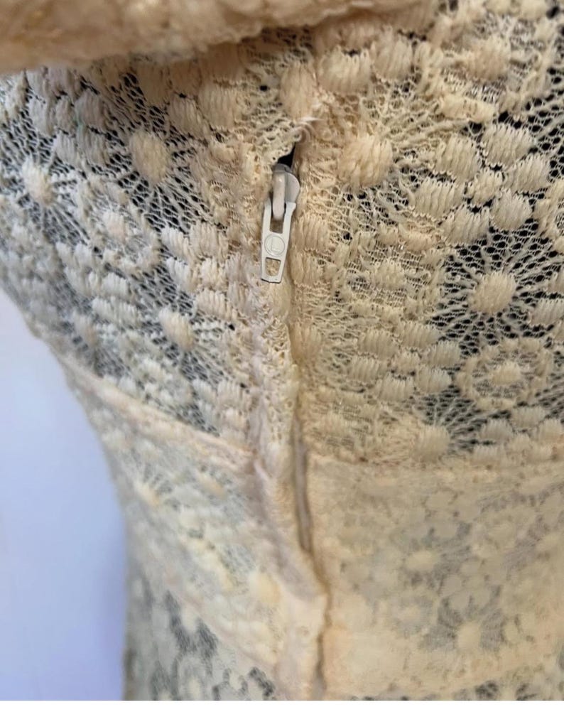 May include: A close-up of a cream-colored lace garment with a zipper running down the back.