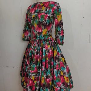 May include: A vintage dress with a colorful abstract print. The dress has a fitted bodice and a full skirt. The print features shades of pink, yellow, green, blue, and brown.