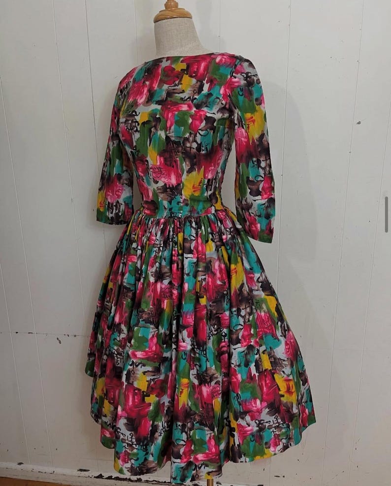 May include: A vintage dress with a colorful abstract print. The dress has a fitted bodice and a full skirt. The print features shades of pink, yellow, green, blue, and brown.