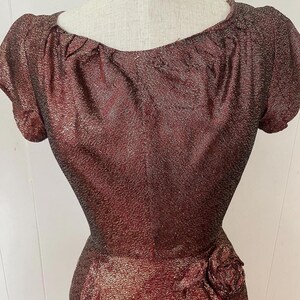 May include: A burgundy and gold sparkly dress with a gathered neckline and a single rose embellishment at the waist.