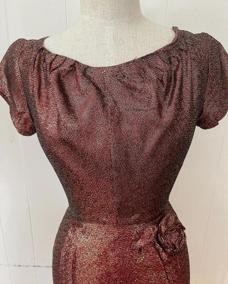 May include: A burgundy and gold sparkly dress with a gathered neckline and a single rose embellishment at the waist.