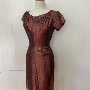 May include: A vintage, short-sleeved, burgundy dress with a sparkly texture and a single rose embellishment at the waist.
