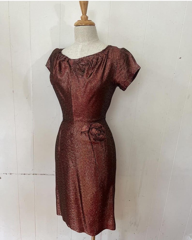 May include: A vintage, short-sleeved, burgundy dress with a sparkly texture and a single rose embellishment at the waist.
