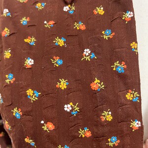 May include: Brown fabric with a small floral pattern in shades of blue, yellow, orange, and white.