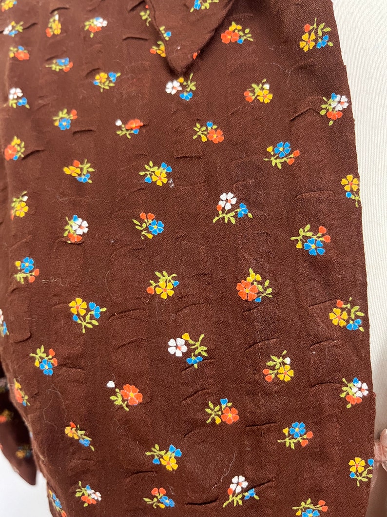 May include: Brown fabric with a small floral pattern in shades of blue, yellow, orange, and white.
