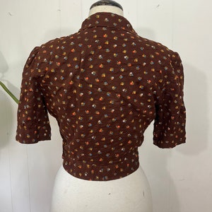 May include: A brown short-sleeved blouse with a small floral print. The blouse has a button-up collar and a fitted waist.