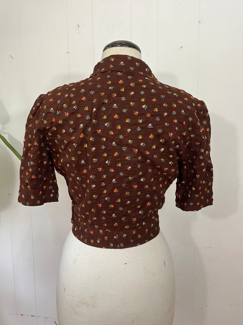 May include: A brown short-sleeved blouse with a small floral print. The blouse has a button-up collar and a fitted waist.