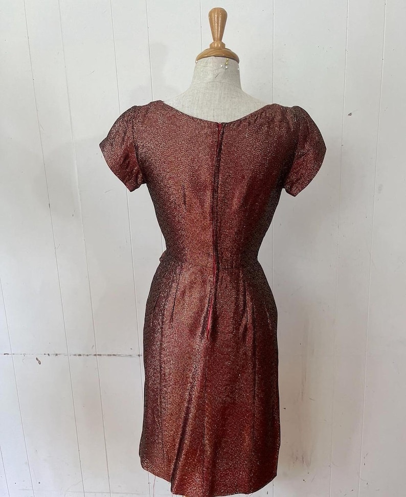 May include: A maroon sparkly dress with a scoop neck and short sleeves. The dress has a back zipper and a fitted silhouette.