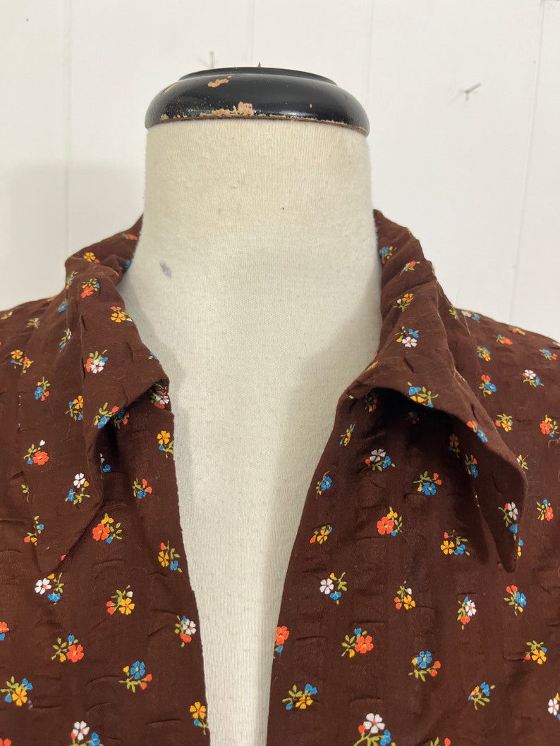 May include: A brown collared shirt with a small floral print in shades of blue, orange, white, and green.