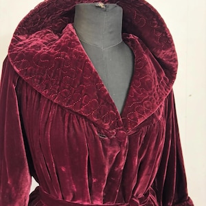 May include: A claret velvet dressing gown with a quilted collar and cuffs. The gown has a matching belt and a button closure. The fabric has a soft sheen, and the design is vintage.