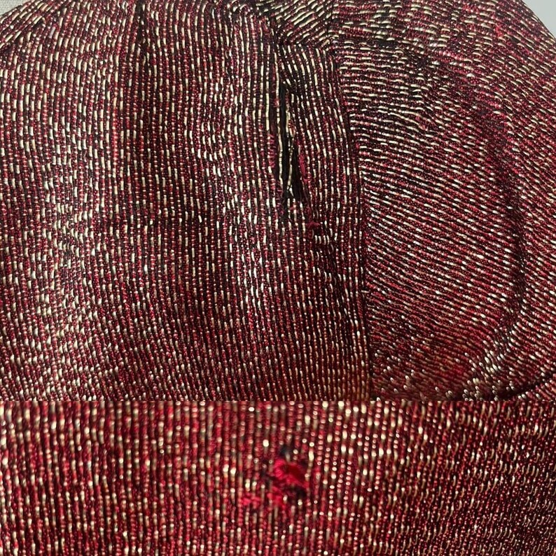 May include: Close-up of a red fabric with a subtle shimmer. The fabric is made of small, tightly woven threads, creating a textured surface.