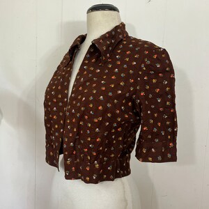 May include: A brown short-sleeved button-up shirt with a small floral print in shades of blue, yellow, and orange.