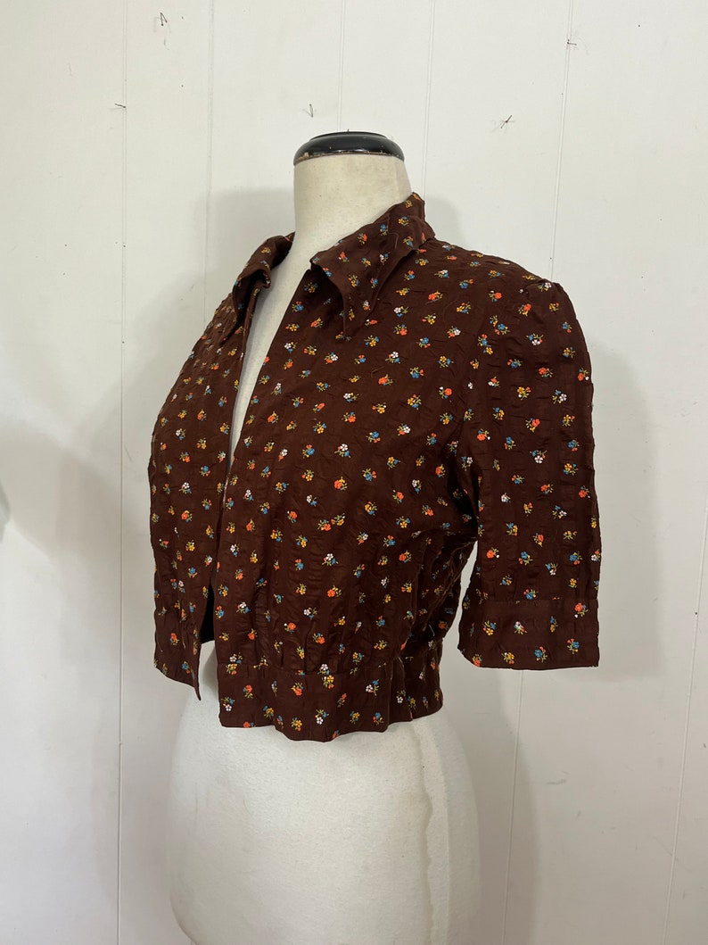 May include: A brown short-sleeved button-up shirt with a small floral print in shades of blue, yellow, and orange.