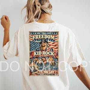 May include: Cream-colored t-shirt featuring a concert poster design. The poster includes the text "FREEDOM" above an image of Kid Rock, with the text "USA FEB 8, 2026" and "TIL YOU CAN'T". The design incorporates the American flag.