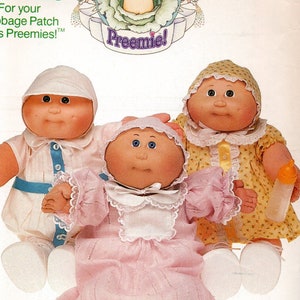 May include: A vintage Butterick pattern envelope featuring three Cabbage Patch Kids Preemie dolls. The dolls are dressed in various outfits, including a pink dress, a yellow floral dress, and a white outfit with blue accents. The envelope has the text "CLOTHES" and "Preemie!"