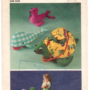 May include: Vintage Simplicity sewing pattern featuring stuffed animal designs. The image shows a pink seal, a blue and white checkered whale, and a green turtle with a yellow patterned shell. The pattern includes instructions for making these plush toys.
