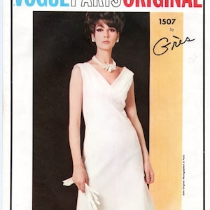 May include: A vintage Vogue Paris Original fashion illustration. The image features a woman in a white sleeveless dress, holding white gloves. The text at the top reads "Vogue Paris Original". The dress has a V-neck and a slightly flared skirt.