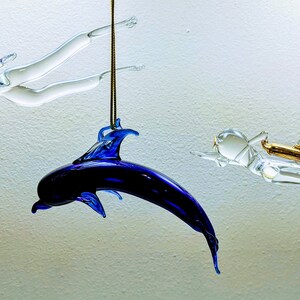 May include: Three glass ornaments hanging from the ceiling. Two are clear glass figures of divers, one with a pink fin and the other with a gold tank. The third ornament is a blue glass dolphin.