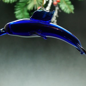 May include: A cobalt blue glass dolphin ornament. The dolphin is in a leaping pose with its tail fin extended.