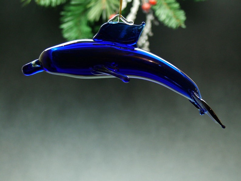 May include: A cobalt blue glass dolphin ornament. The dolphin is in a leaping pose with its tail fin extended.