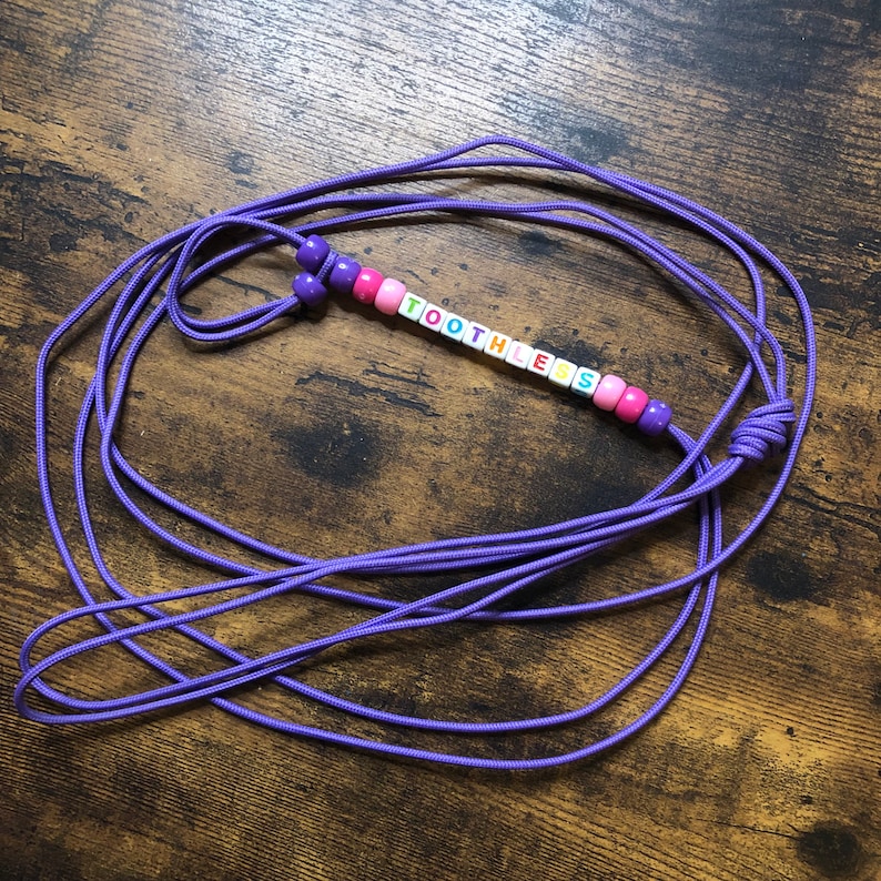 May include: Purple cord necklace with colorful letter beads spelling "TOOTHLESS".