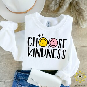 May include: White sweatshirt with the text "Choose Kindness" in black lettering. The text is surrounded by two smiley faces, one yellow and one pink.