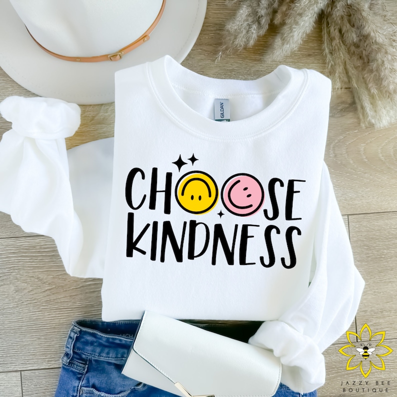 May include: White sweatshirt with the text "Choose Kindness" in black lettering. The text is surrounded by two smiley faces, one yellow and one pink.
