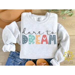 May include: A gray sweatshirt with the text "dare to DREAM" in colorful letters with a pattern on each letter. The letters are outlined in black.