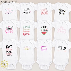 Pu&ograve; includere: Body per neonati bianchi con vari disegni grafici e testo colorati. I disegni includono frasi come "Born to Sparkle", "Hello World", "Little Lovebug" e "Eat Sleep Poop Repeat". L'immagine include anche un logo per Jazzy Bee Boutique.