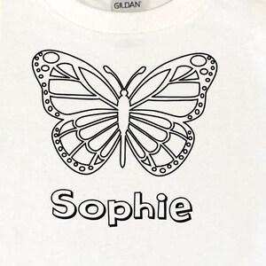May include: White t-shirt with a black outline of a butterfly and the name "Sophie" printed below it.