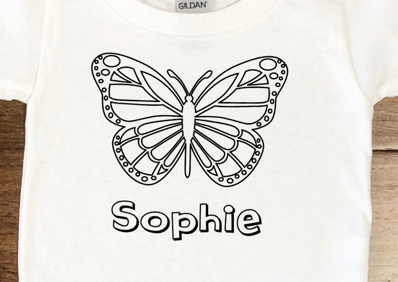 May include: White t-shirt with a black outline of a butterfly and the name "Sophie" printed below it.