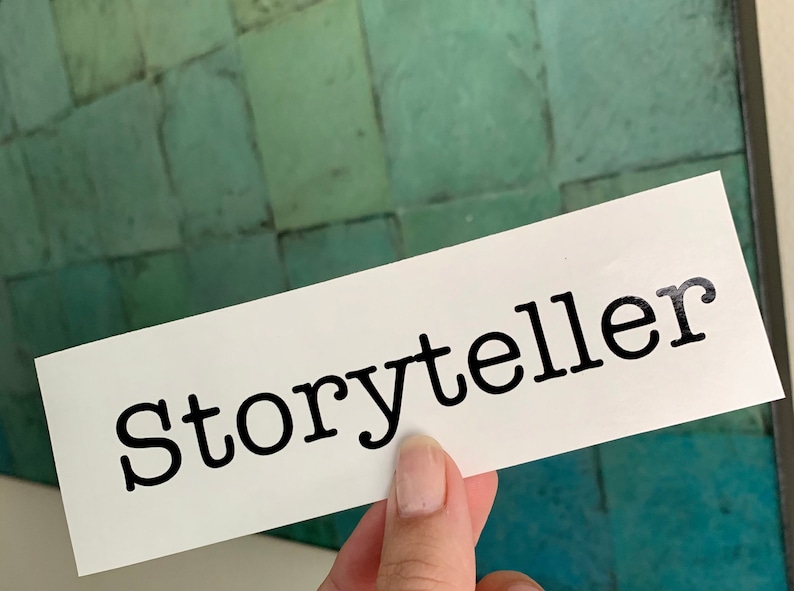 Pode incluir: Cart&atilde;o branco com a palavra "Storyteller" impressa em preto em fonte de m&aacute;quina de escrever.