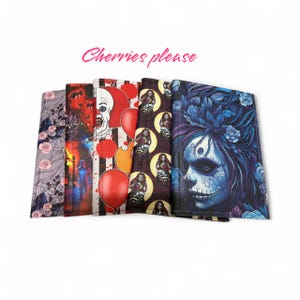 Peut inclure: Présentation de cinq portefeuilles aux motifs variés. L'un présente un motif floral, un autre une scène d'horreur, et un troisième un clown avec un ballon rouge. Le texte "Cherries please" est écrit en rose en cursive.