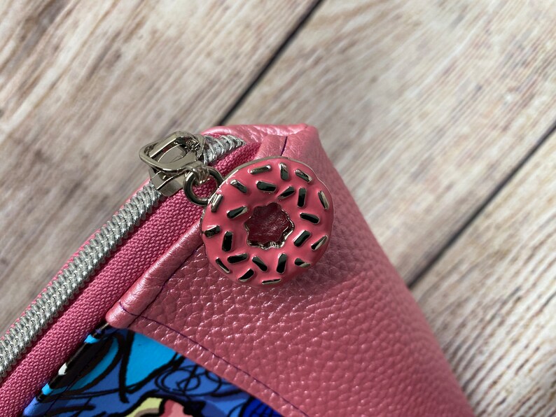 May include: A pink zippered pouch with a donut-shaped zipper pull. The donut is pink with white sprinkles.